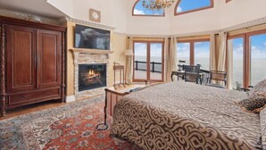 Une chambre spacieuse avec un grand lit, une cheminée, un balcon avec vue sur la mer et un lustre.