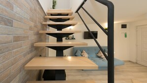 Un escalier moderne avec des marches en bois et des rampes noires, menant à un espace de vie comprenant un canapé et un téléviseur à écran plat.