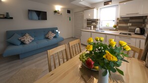 Un salon moderne avec un canapé bleu, une table à manger en bois et un vase rempli de fleurs jaunes.