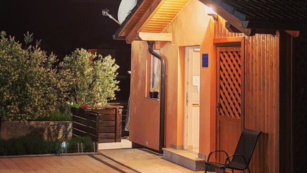 Un bâtiment bien éclairé, avec une façade en bois, une entrée couverte et une chaise placée à l’extérieur.