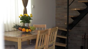 Un coin repas avec une table en bois, des chaises, un panier de fruits et un vase de fleurs.