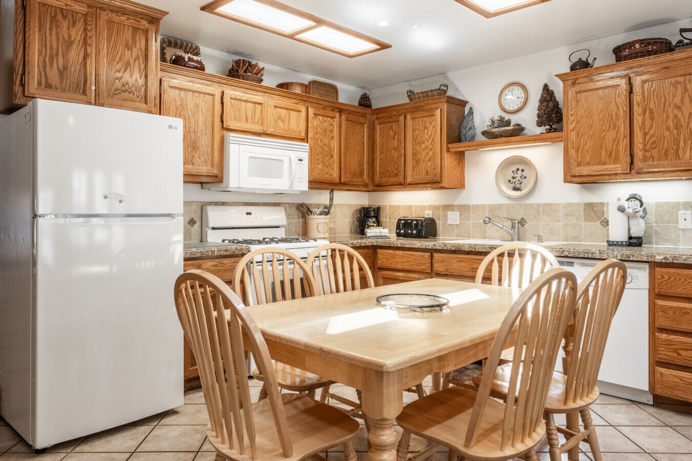A kitchen with wooden cabinets, a white refrigerator, a microwave, a stove, and a dining table with four chairs.