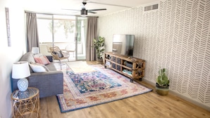 A modern living room with a grey sofa, a patterned rug, a wooden entertainment unit, and a ceiling fan. - Desert Modern Old Town Oasis | Fresh Renovation! | Walk to Restaurants & Bars (Scottsdale)