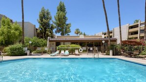 A swimming pool with lounge chairs, surrounded by palm trees and a building with a flat roof. - Desert Modern Old Town Oasis | Fresh Renovation! | Walk to Restaurants & Bars (Scottsdale)