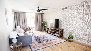 A modern living room with a grey sofa, a patterned rug, a wooden TV stand, and a ceiling fan. - Desert Modern Old Town Oasis | Fresh Renovation! | Walk to Restaurants & Bars (Scottsdale)