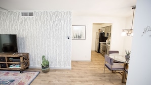 A modern living room with a herringbone-patterned wall, a flat-screen TV, a wooden entertainment unit, a potted plant, and a colorful rug. - Desert Modern Old Town Oasis | Fresh Renovation! | Walk to Restaurants & Bars (Scottsdale)