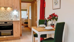 A modern kitchen with wooden cabinets, a built-in oven, and a dining area with a table set for two. - The Old Inverchroskie Kennels (Enochdhu, near Pitlochry)