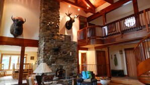 A spacious lobby with a stone fireplace, leather seating, and a balcony with wooden railings.