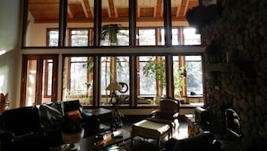 A spacious living room with a high ceiling, large windows, and a stone wall.