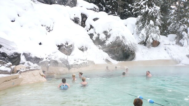 A hot spring area with clear water, surrounded by snow-covered rocks and trees.