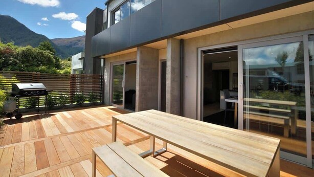 A modern house with a patio, a wooden table, and a grill.