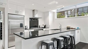 A modern kitchen with a stainless steel refrigerator, a gas stove, and a black countertop island with bar stools.