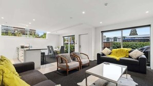 A modern living room with a sofa, armchairs, a coffee table, and a dining area with a table and chairs.