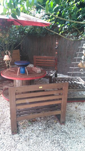 Relax in a serene outdoor space with a bench, table, and barbecue grill, surrounded by lush greenery.