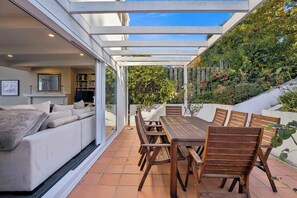 Eine moderne Terrasse mit Esstisch und Stühlen, einer Sitzecke und einem Kamin.