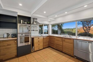 A modern kitchen with built-in appliances, a large window, and a view of trees.
