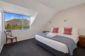 A bedroom with a large window, a bed with pillows, a chair, and a nightstand.