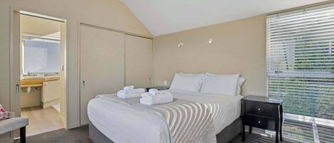 A hotel room with a bed, bedside table, and a window with blinds.