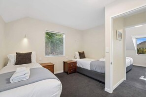 Ein Hotelzimmer mit zwei Betten, einem kleinen Schreibtisch, einem Fenster mit Jalousien und einer Tür zu einem weiteren Raum.