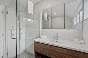 A modern bathroom with a glass-enclosed shower, a large mirror, and a wooden vanity.