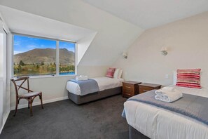 A bedroom with two beds, a window with a mountain view, a chair, and a nightstand.