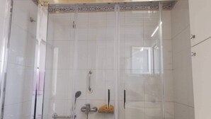 Casa de banho moderna com cabine de duche em vidro, azulejos brancos e um pequeno armário com produtos de higiene pessoal.