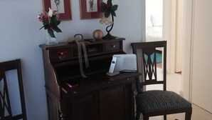 Quarto com um armário de madeira, duas cadeiras, uma mesinha com uma planta e várias fotos emolduradas na parede.