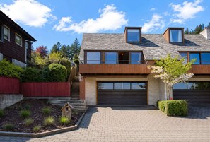 A modern two-story house with a garage, a wooden deck, and a landscaped garden.