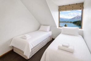 A bedroom with two beds, a window with a view of a lake and mountains, and a sloped ceiling.