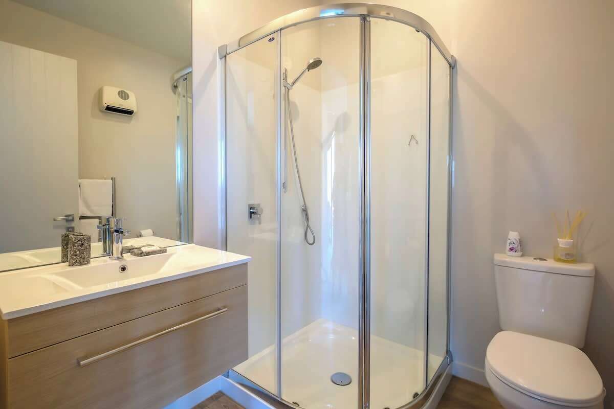 A modern bathroom with a glass-enclosed shower, a white sink with a marble countertop, and a toilet with a tissue dispenser.