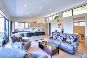 A modern living room with a grey sofa set, a coffee table, and a dining area with chairs.