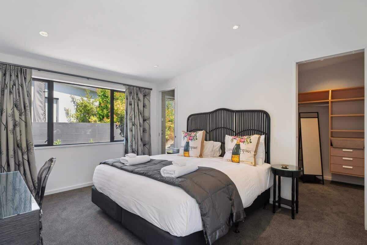 A modern bedroom with a large bed, a bedside table, a wardrobe, and a window with curtains.