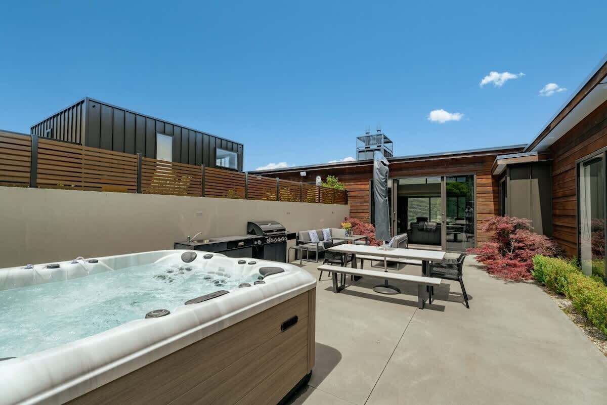 A modern outdoor patio with a hot tub, barbecue grill, and outdoor seating area.