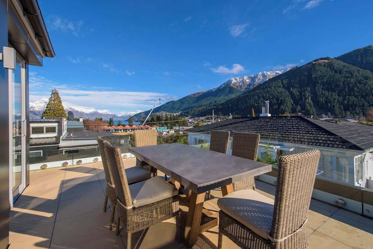 A terrace with wicker furniture and a table, overlooking a mountainous landscape with a clear sky.