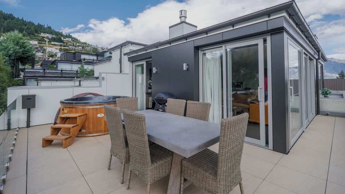Een modern terras buiten met een eettafel, rieten stoelen en een jacuzzi.