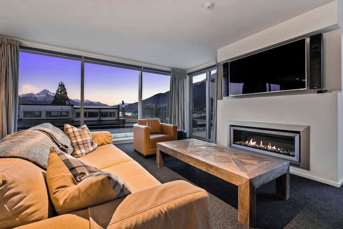 A modern living room with a sofa, armchair, and coffee table, a fireplace, and large windows with a mountain view.