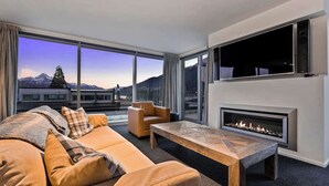 A modern living room with a sofa, armchair, and coffee table, a fireplace, and large windows with a mountain view.