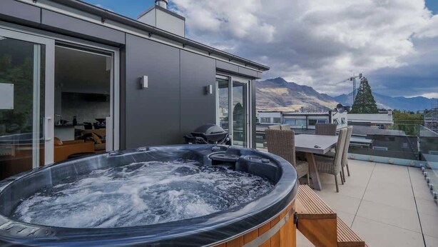 A hot tub on a balcony with a mountain view, a sliding glass door, and a table with chairs.