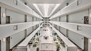 Un vaste atrium doté d’un haut plafond et d’un espace central ouvert, aménagé avec des coins salon et des plantes en pot.