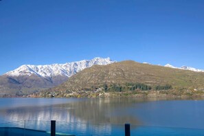 A mountain range with snow-capped peaks in the background, a calm lake in the foreground, and a small settlement with houses along the lakeshore.