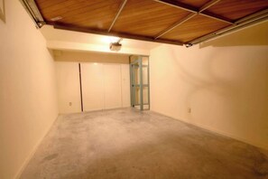 A room with a concrete floor, wooden ceiling beams, and a door leading to another room.