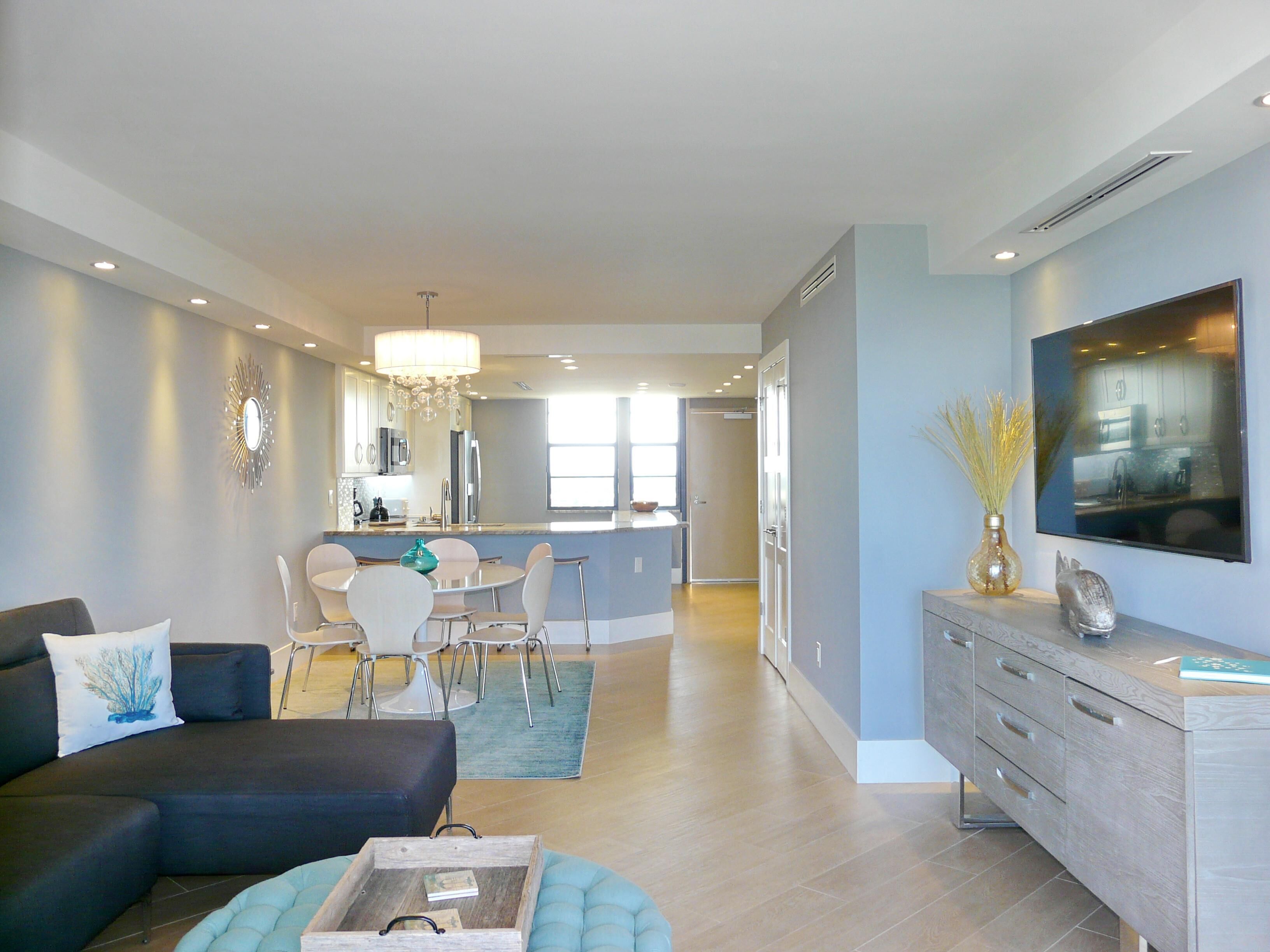 Een moderne woonkamer met een bank, een salontafel en een eethoek met stoelen en een kroonluchter.