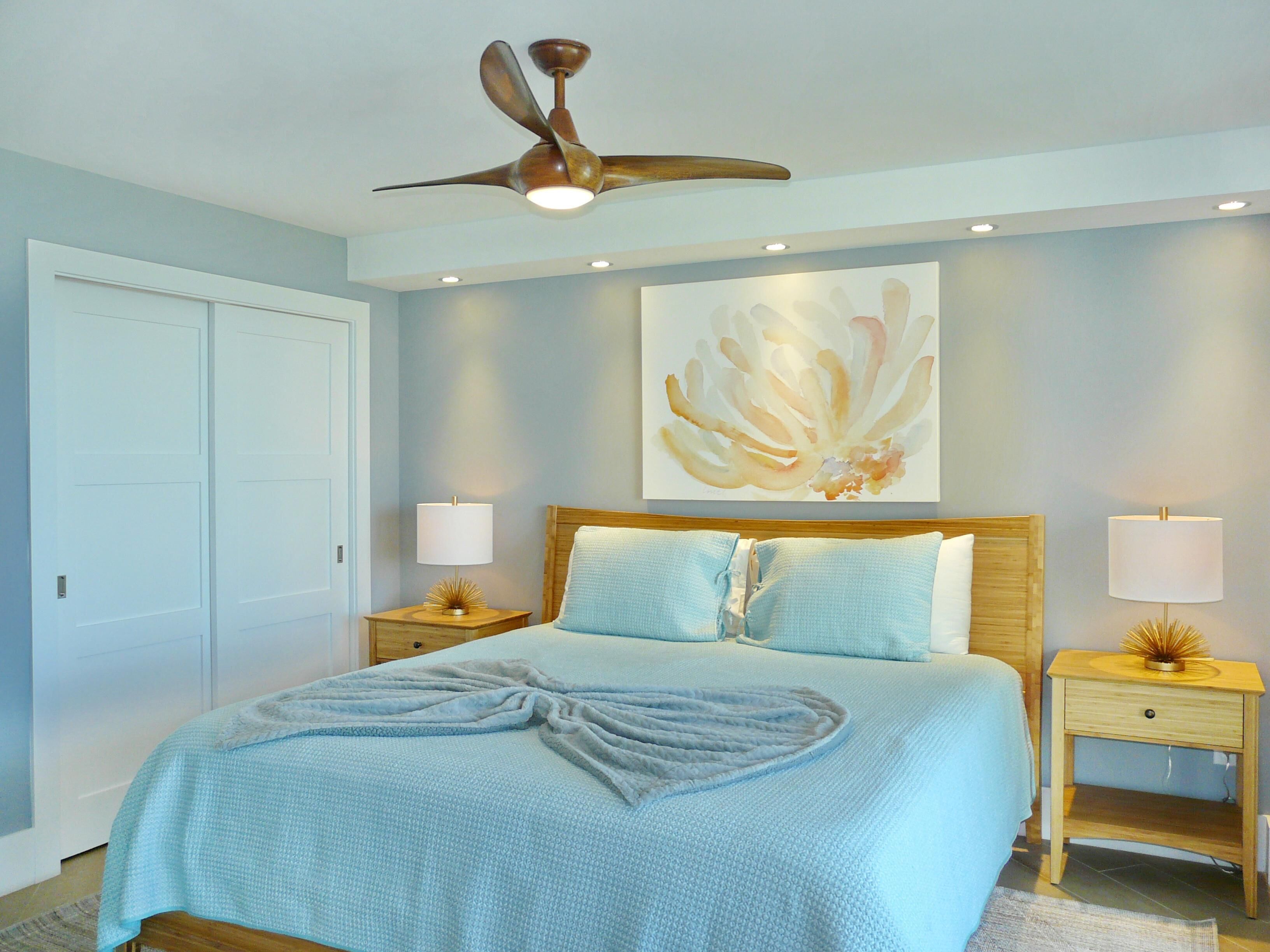 A bedroom with a bed, two bedside tables, a ceiling fan, and a wall art piece.