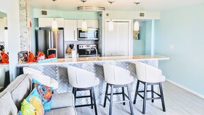 A modern kitchen with a herringbone tile backsplash, stainless steel appliances, and a bar area with white barstools.