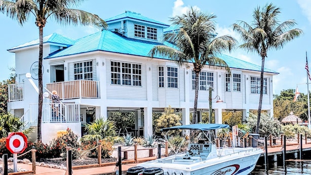 A waterfront property with a boat docked in front, a building with a blue roof, and palm trees.