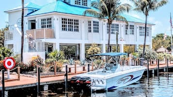 A waterfront property with a boat docked in front, a building with a blue roof, and palm trees.