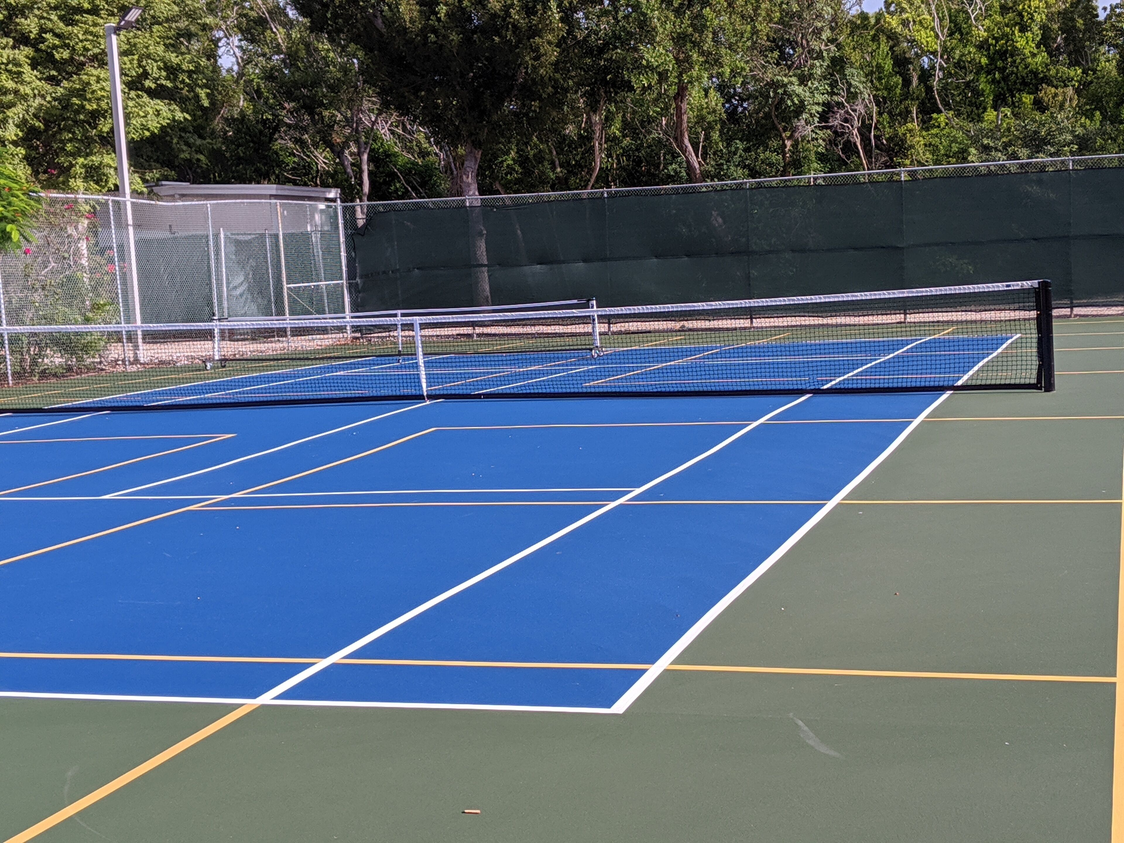 A tennis court with a net, surrounded by a fence and trees.
