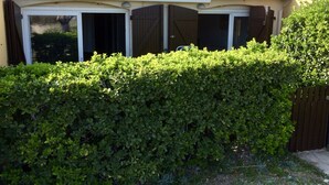 A house with a tiled roof, a covered porch with glass doors, and a well-maintained hedge.