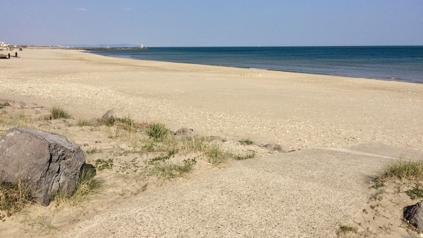 A wide sandy beach with a clear blue sky and calm sea.