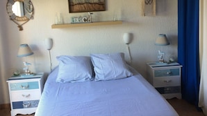 A bedroom with a bed, two nightstands, a wall-mounted shelf, a painting, and a decorative mirror.